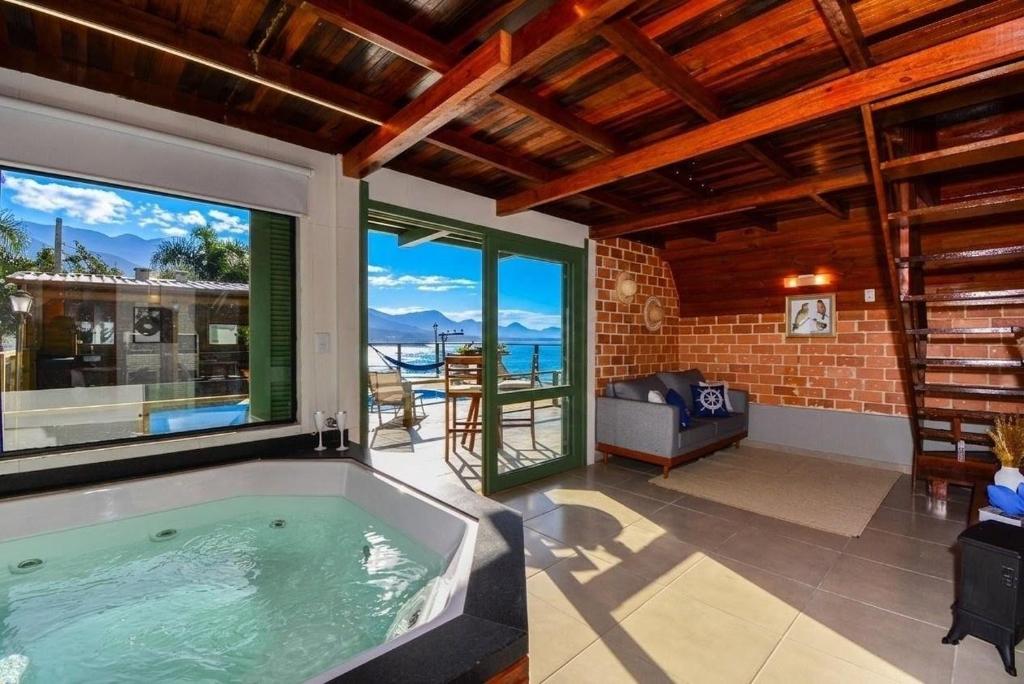 a bath tub in a room with a large window at Chalé com Jacuzzi e Vista Mar - PLH007 in Palhoça