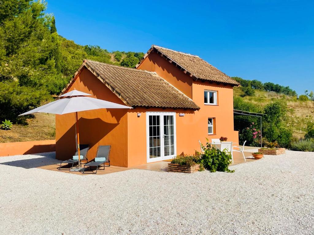 a small orange house with an umbrella and chairs at Casita Tierra De Suerte in Pizarra