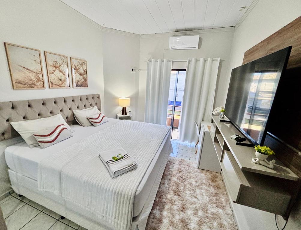 a white bedroom with a large bed and a television at Hospedagem Domiciliar em Lucas do Rio Verde in Lucas do Rio Verde