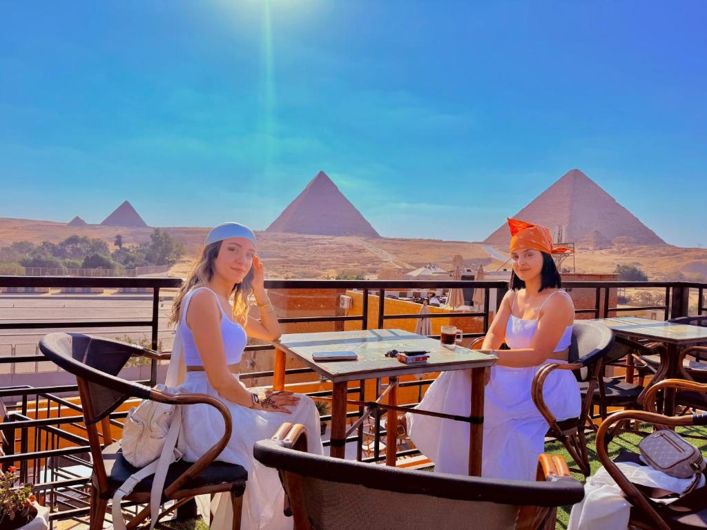two women sitting at a table with pyramids in the background at Dima Plaza Pyramids View in Cairo