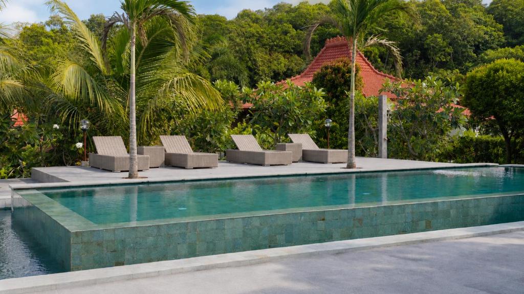 a swimming pool with lounge chairs and palm trees at Mirabelle Joglo Village in Karimunjawa
