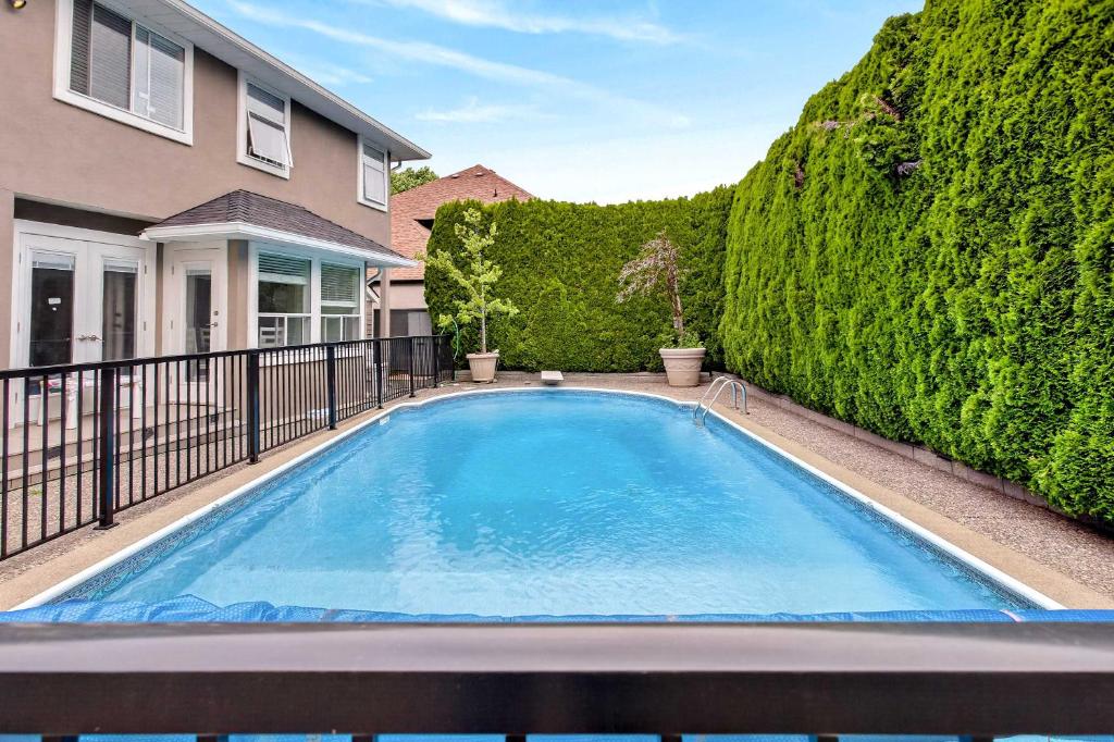 a swimming pool in front of a house with a hedge at Surrey Two Bedroom Suite with Pool Access in Surrey