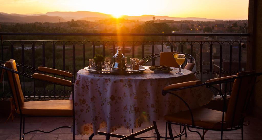 a table with wine glasses on a balcony with the sunset at Dar Amoudou in Ouarzazate