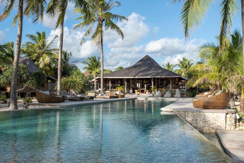 a swimming pool in a resort with palm trees at Seed Resort in Nembrala