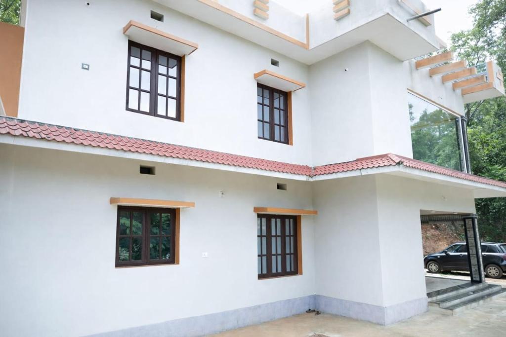 a white house with a car parked in the driveway at Sindu Homestay in Kalasa