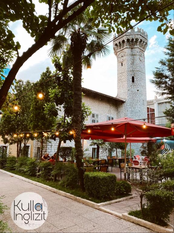 a building with a tower with a table and an umbrella at The Englishman's Clock Tower Hostel & More in Shkodër