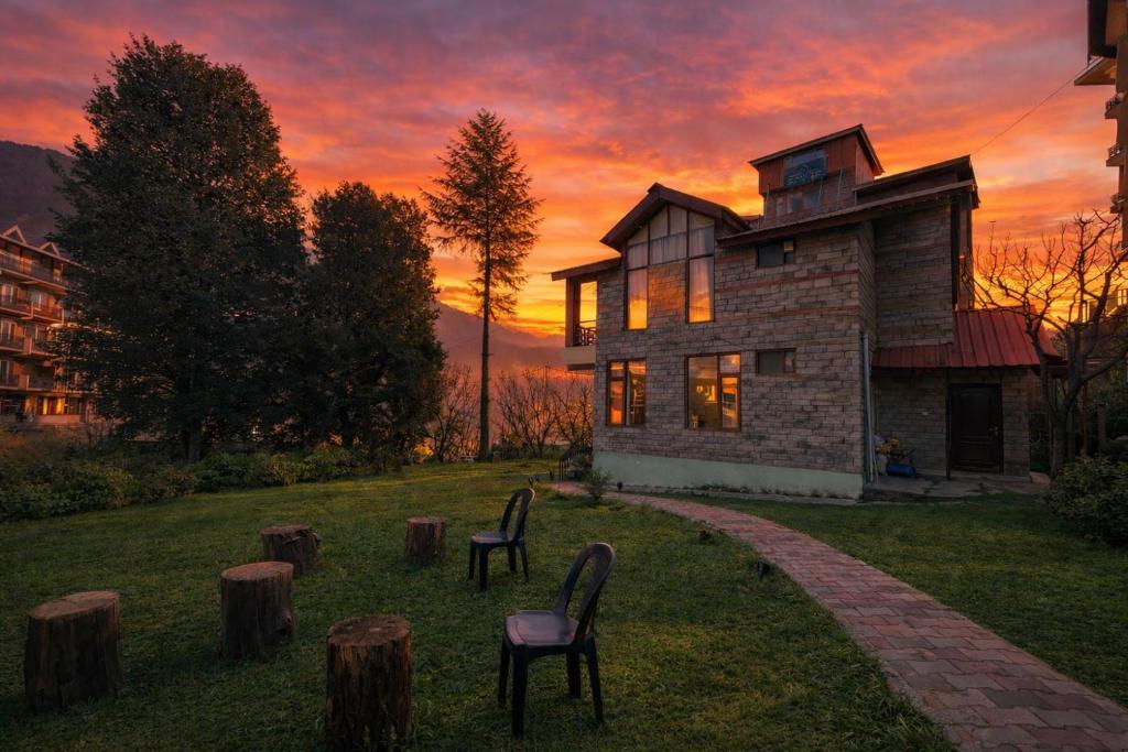 a house with two chairs in front of a sunset at 4 Bedroom Luxury Bungalow In Manali With Beautiful Scenic Mountain & Orchard View - #Private Bungalow #Premium Big rooms #Parking #Guest Preferred in Manāli