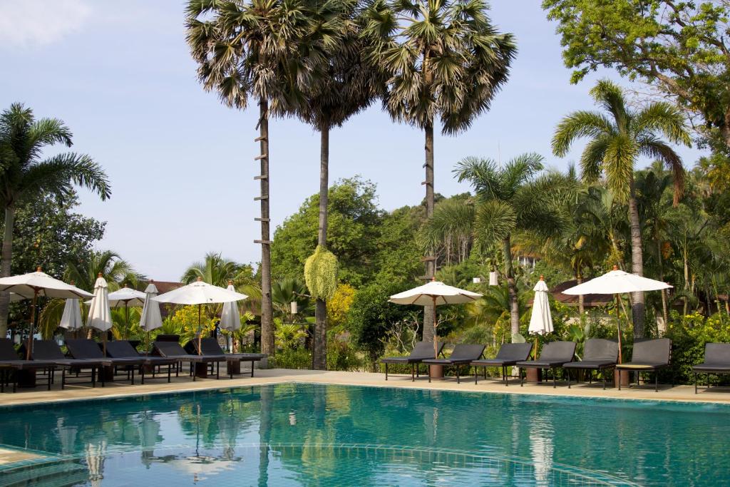 a swimming pool with chairs and umbrellas and palm trees at Anda Lanta Resort in Ko Lanta