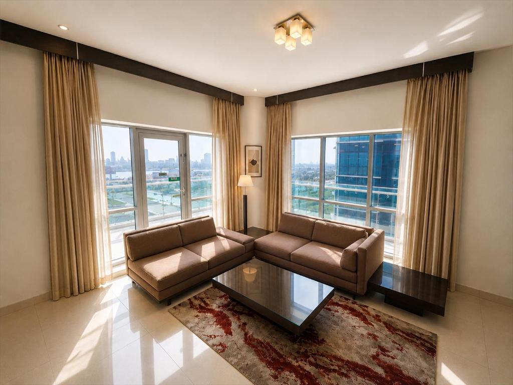 a living room with a couch and a table and windows at Tulip Creek Hotel Apartments in Dubai