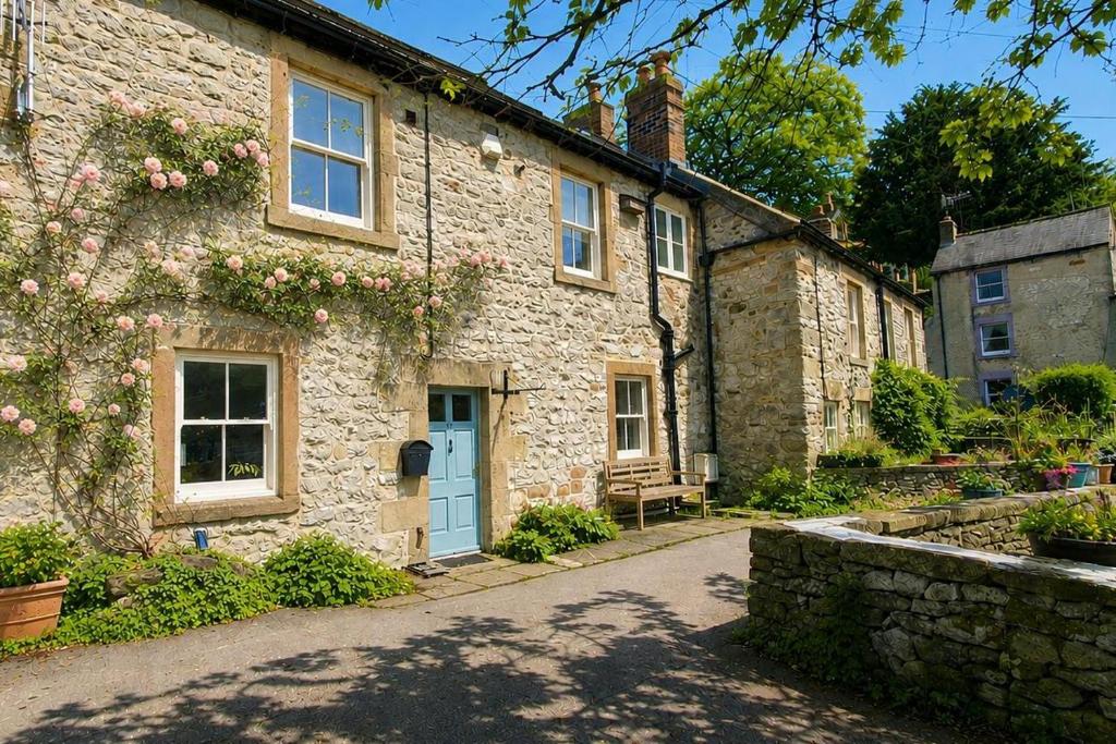 a stone house with a blue door on a street at Bakers Yard Cottage, Bonsall, Peak District in Bonsall