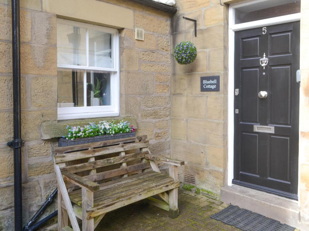 a wooden bench sitting outside of a building with a window at Bluebell Cottage in Alnwick