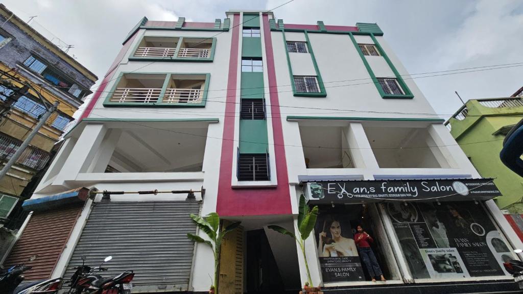 a tall white and green building with a store at Akshay Guest House in Krishnanagar