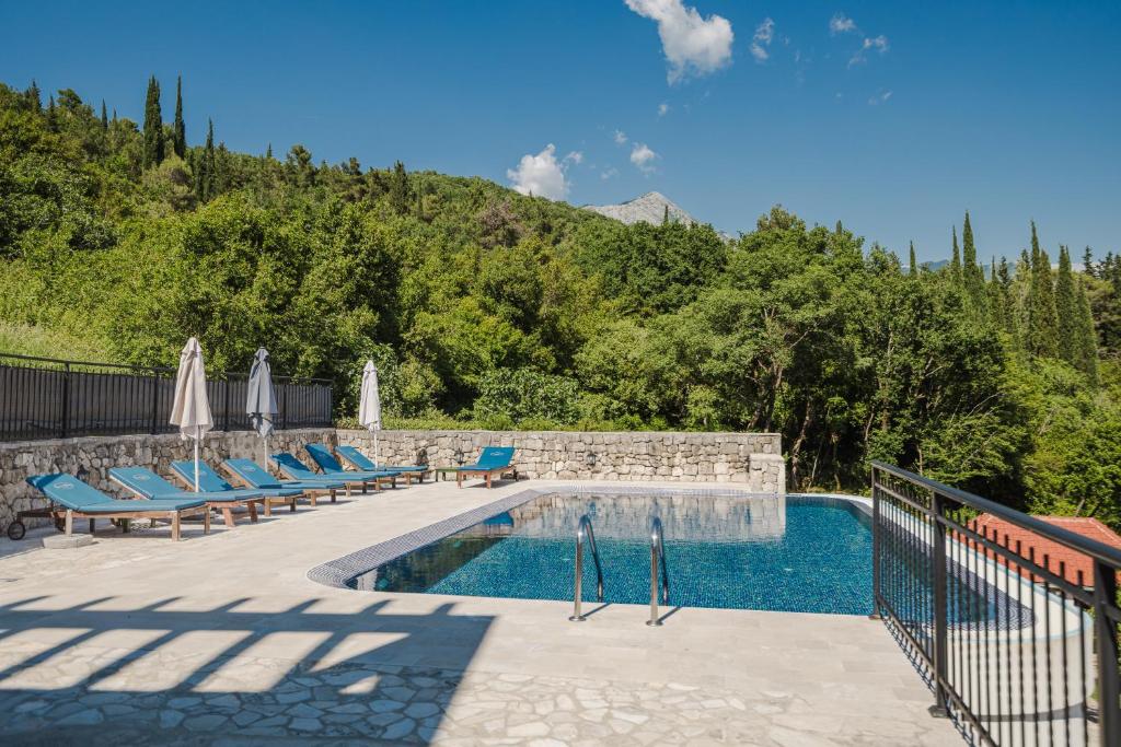 a swimming pool with blue lounge chairs next to a mountain at Lavender house with shared pool in Herceg-Novi