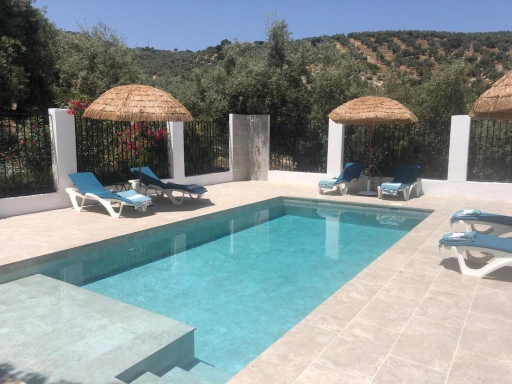 a swimming pool with blue chairs and umbrellas at Stunning views, 3 bed, private pool, olive grove in Iznájar