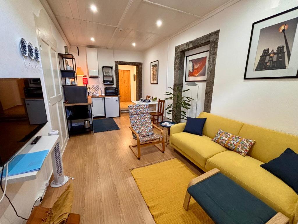 a living room with a yellow couch and a kitchen at Casinha do Solar in Angra do Heroísmo