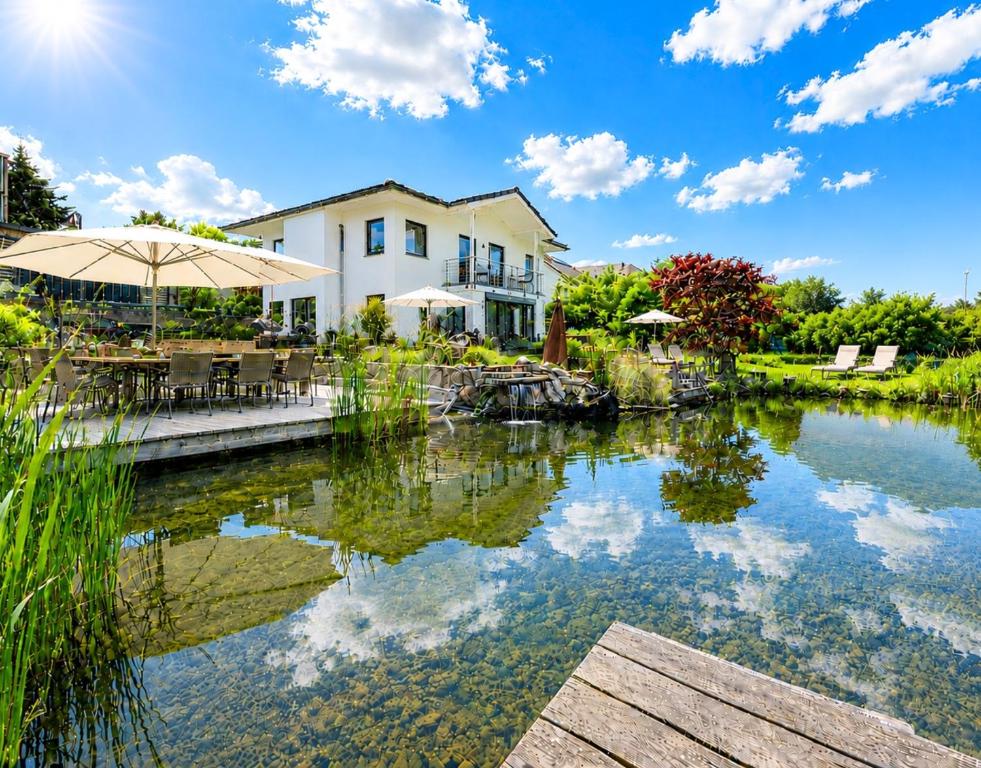 a house and a pond with an umbrella at Schäfers - Ihr Wohlfühlort, Ferienwohnungen & Ferienhaus am Naturteich an 2 Seen bei Leipzig in Großpösna
