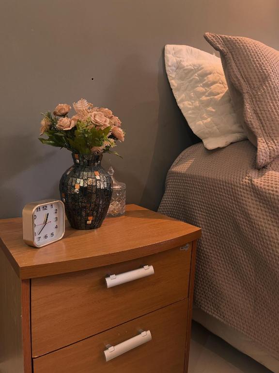 a table with a clock and a vase with flowers on it at Apartamento Charmoso e Tranquilo para sua Estadia in Vargem Alta