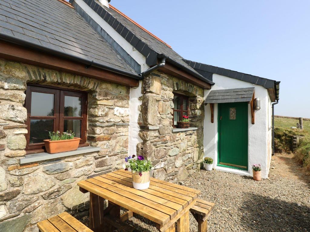 a stone cottage with a wooden table and a green door at Ysgol Hill Cottage in Rosebush