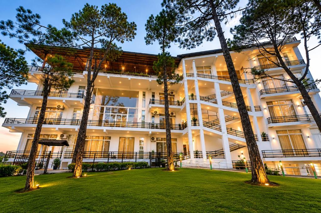 a large white building with trees in the foreground at Eva & Era Paradise in Solan