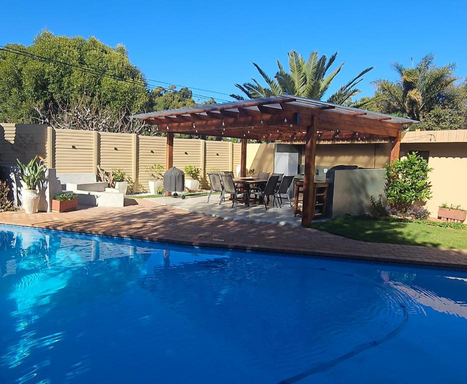 a swimming pool with a wooden pergola and a patio at Rest-a-While Guest House - Pretoria in Pretoria
