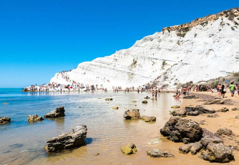 a group of people on a beach next to a mountain at WHITE COAST APARTMENTS - Family Stays and Free Parking in Realmonte