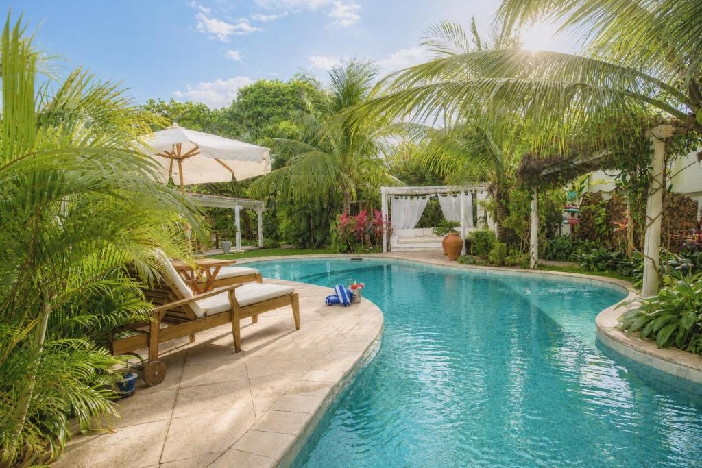 a swimming pool with two chairs and palm trees at Pousada Ilha do Vento in São Miguel do Gostoso