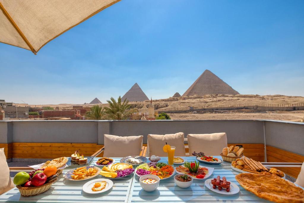a table full of food with the pyramids in the background at The Stay Pyramids Inn in Cairo
