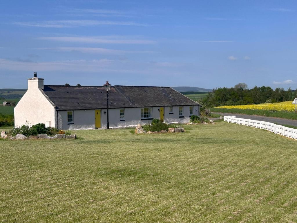 a white house with a large field in front of it at Calsie Cottage, Clatt in Kirktown of Clatt