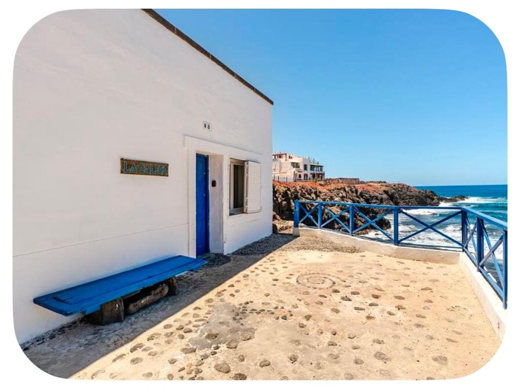 a white building with a blue door next to the ocean at Ocean front surf House El Cotillo in El Cotillo