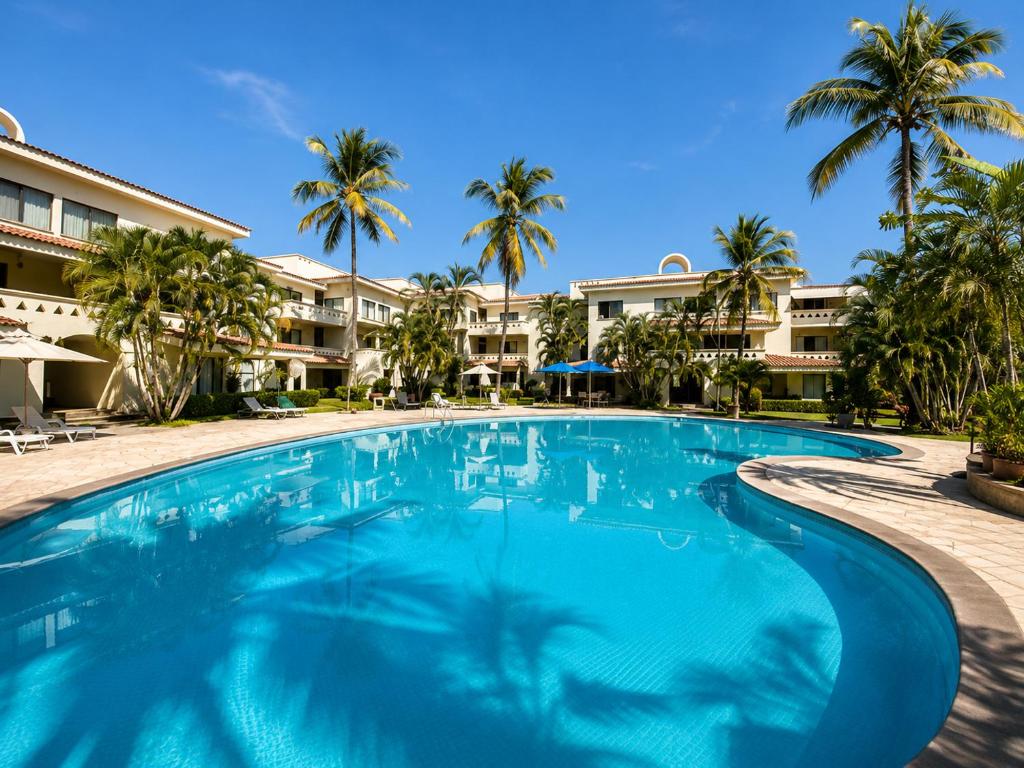 a swimming pool with palm trees and condos at Hermoso apartamento en Manzanillo con alberca y cancha de tenis, Ideal para relajarse y disfrutar de una escapada tranquila en el paraíso tropical in Manzanillo