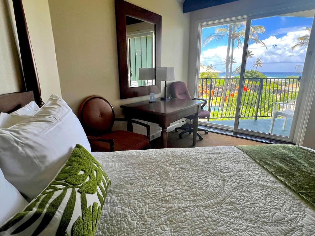 a bedroom with a bed and a desk with a view of the ocean at Oceanview Studio at Kauai Beach Resort #2444 in Lihue