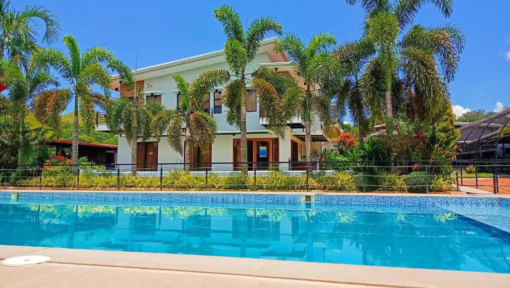 a swimming pool in front of a house with palm trees at Casa De Española Hotel and Resort in Aritao
