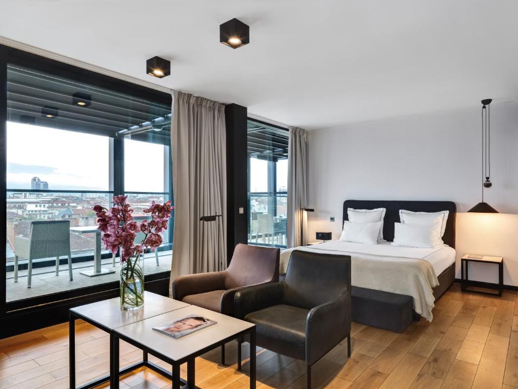 ソフィアにあるSense Hotel Sofia, a Member of Design Hotelsのベッド、ソファ、テーブルが備わるホテルルームです。