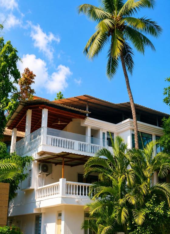 a white building with a balcony and a palm tree at Coconut Sky 2Bhk Penthouse Baga in Baga
