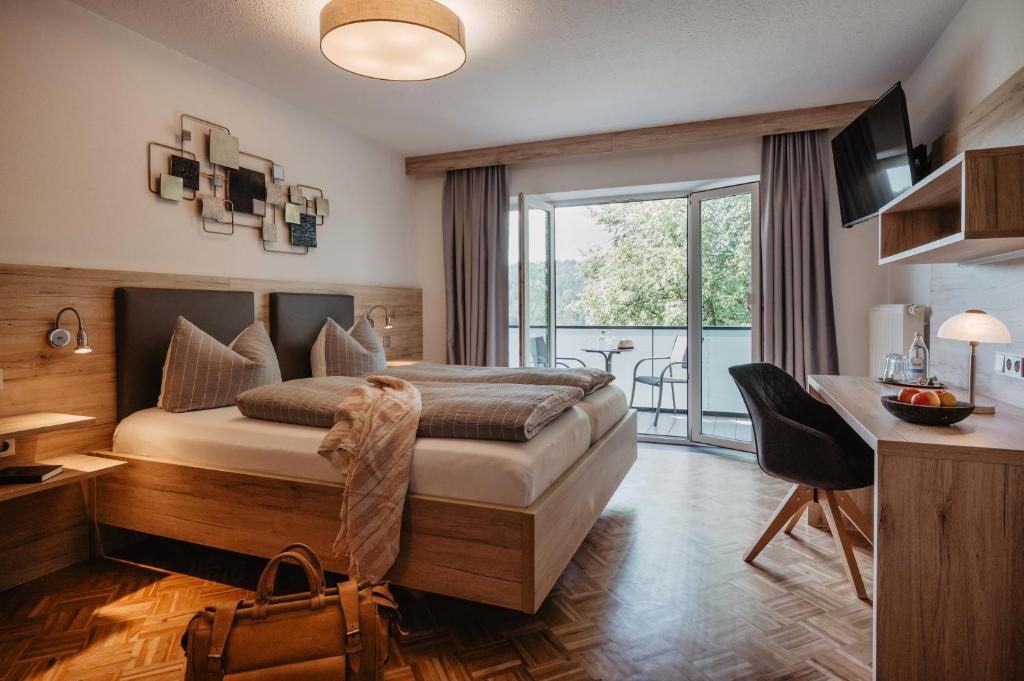a bedroom with a bed with a desk and a balcony at Hotel am Haidel in Hinterschmiding