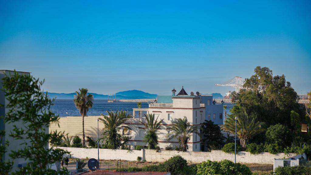 a white building with palm trees and the ocean at Maison d'hôtes Kamilia in Ksar es Sghir