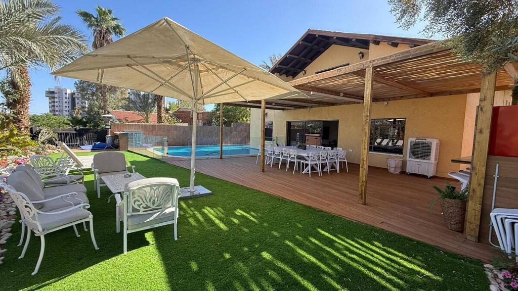 a patio with chairs and an umbrella and a pool at Villa Sun Bay in Eilat