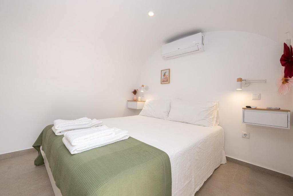 a bedroom with a bed with white sheets and a green blanket at Casa Flora Tiny House in Fuzeta