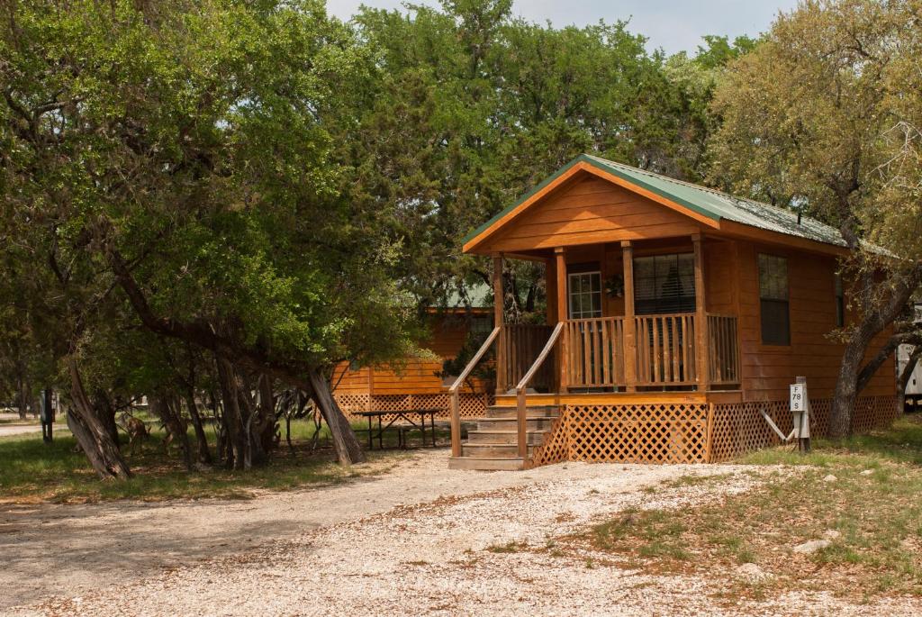 une cabane dans les bois avec une véranda et des arbres dans l'établissement Medina Lake Camping Resort Cabin 4, à Lakehills