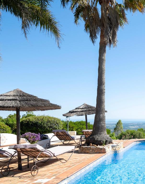 ein Schwimmbad mit Liegestühlen, Sonnenschirmen und Palmen in der Unterkunft Monte Borboleta - Villas, Apartments in Faro