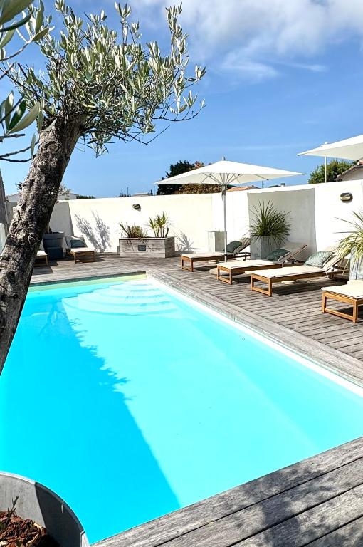 a blue swimming pool with lounge chairs and a tree at Fleur de Ré in Loix