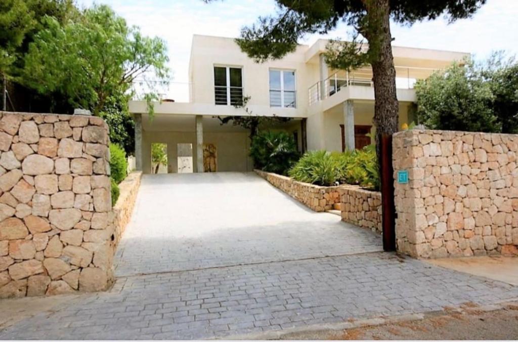 a house with a stone wall and a driveway at Wonderful Villa Cala Tarida in Sant Josep de sa Talaia