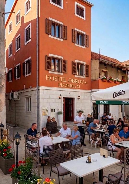 a group of people sitting at tables in front of a building at Hostel Obrovac in Obrovac
