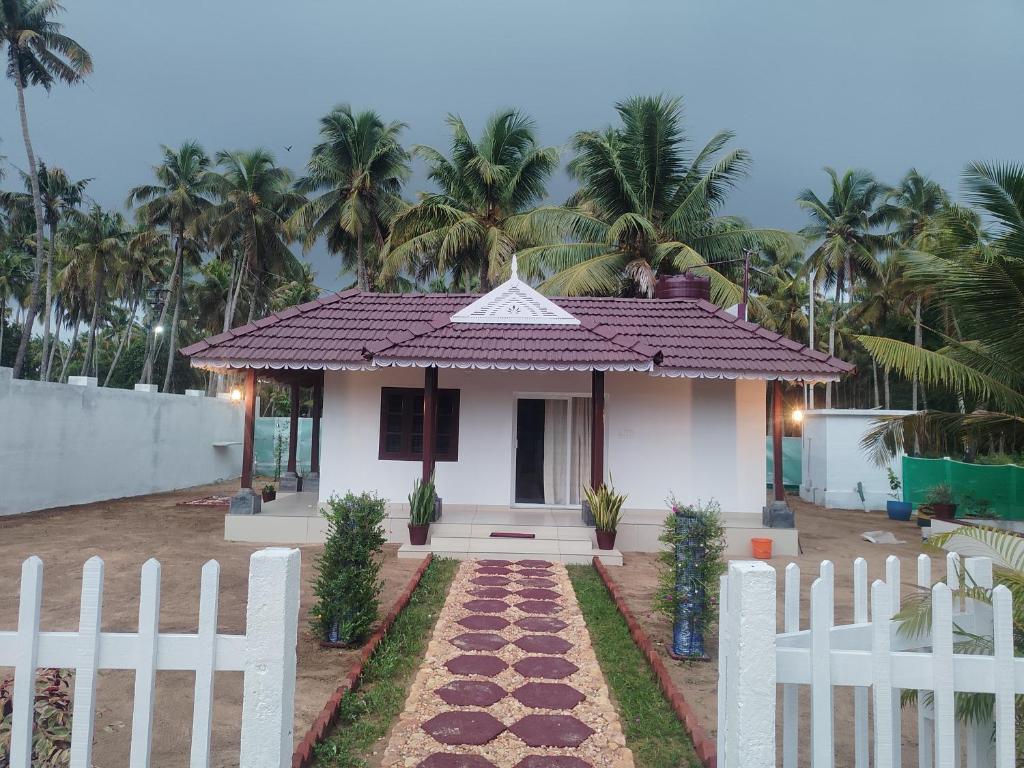 a small white house with a fence and palm trees at Ocean wings Traditional beach villa in Kaipamangalam