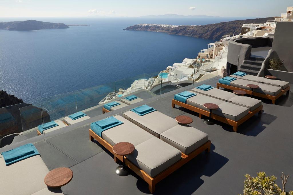 a row of beds on a patio overlooking the ocean at Kivotos Santorini - Preferred Hotels & Resorts in Imerovigli