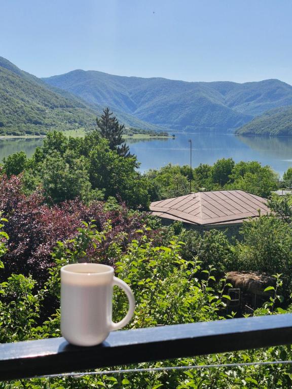 a cup of coffee sitting on a railing overlooking a lake at Ananuri Veranda-Guest House in Ananuri