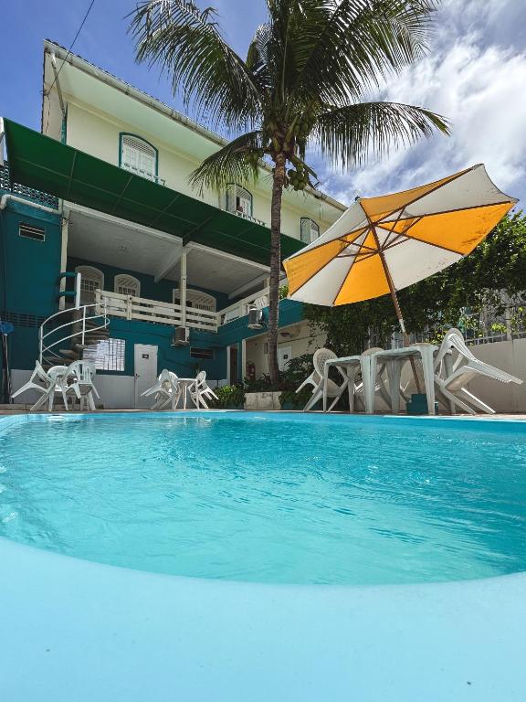 a pool with an umbrella and chairs and a house at Pousada Nossa Natal in Natal