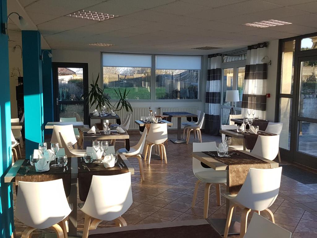 un restaurante con sillas blancas, mesas y ventanas en Logis Hotel- Restaurant La Haie Des Vignes Séminaires et Evènementiel, en Allain