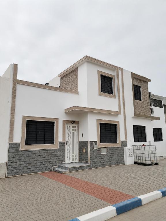 a white building with black shuttered windows on a street at Mini Villa alhoceima in El Arba de Trougout