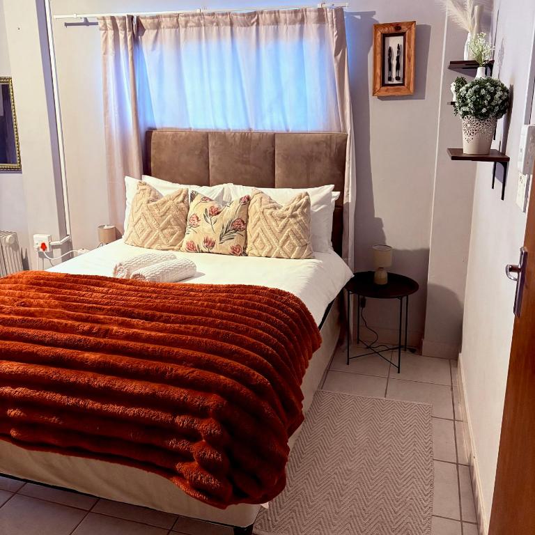 a bedroom with a large bed with a orange blanket at The Nest- on Knowling Street in Grahamstown